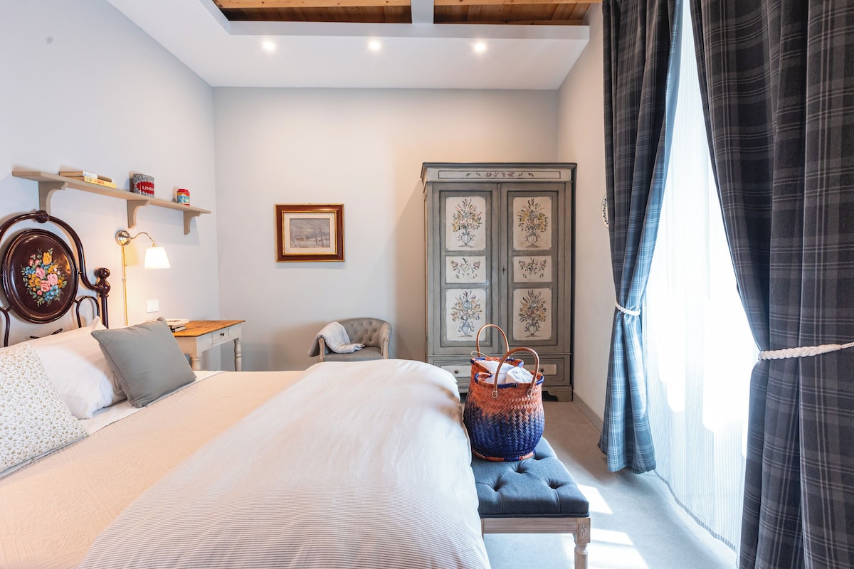 Un dormitorio con cama, mesita de noche, lámpara, silla, armario y ventana con cortinas.