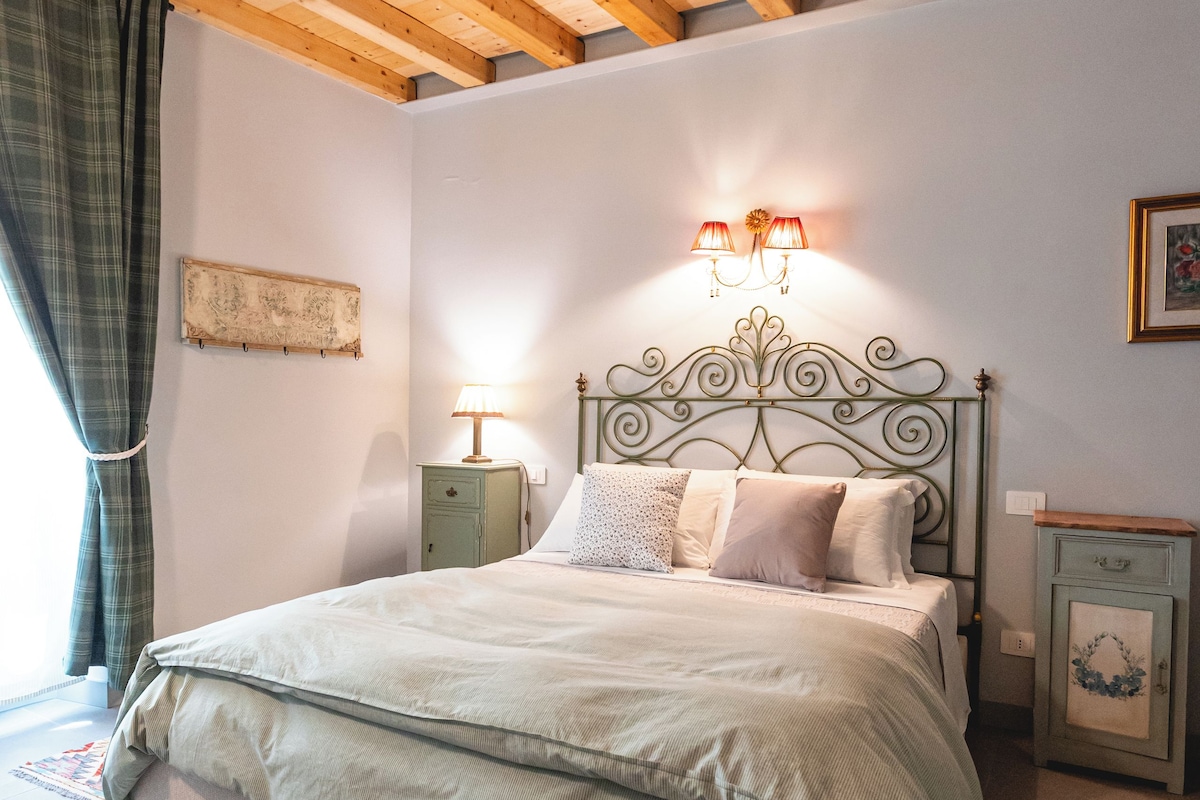 Un dormitorio con cama, mesitas de noche, una lámpara de pared y techo con vigas de madera.
