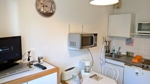 A compact kitchenette with a microwave, a coffee maker, and a small dining area with a chair. - Quiet Studio in Lamalou – 10 min from Thermal Baths – Wi-Fi – Pets Welcome (Lamalou-les-Bains)