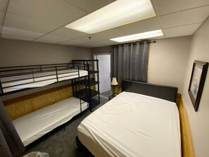 A hotel room with bunk beds, a single bed, a door, a lamp, and a framed picture on the wall. - Winterplace condo lodge - Ski in Ski out (Raleigh County)