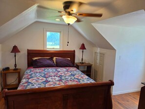 Een slaapkamer met een houten bed, een plafondventilator, twee bedlampen, een raam en een deur.