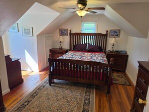 A bedroom with a sloped ceiling, a wooden bed, two bedside tables with lamps, a nightstand, a rug, and a ceiling fan. - Ashwood Acres - 5 minutes from Winterplace!  11 Acres of room to play! (Ghent)