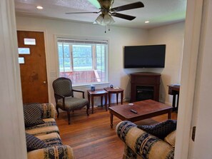 A living room with a ceiling fan, a fireplace, a television, and a large window. - Ashwood Acres - 5 minutes from Winterplace!  11 Acres of room to play! (Ghent)