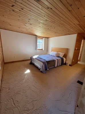 Ein Schlafzimmer mit Holzboden, einem Einzelbett mit gemusterten Bettwaren, einem Fenster mit Vorhängen und einer Tür.