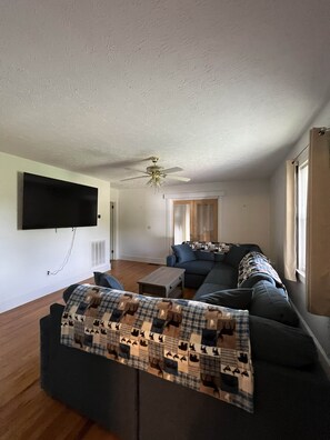 Ein Wohnzimmer mit einem dunkelgrauen Sofa, einer gemusterten Decke, einem Deckenventilator und einem flachbildfernseher, der an der Wand angebracht ist.