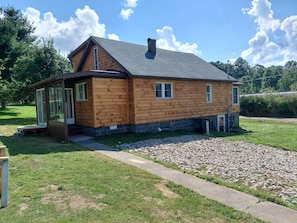 Eine Holzhütte mit einer Laube, einem Schornstein und einer Schotterzufahrt.