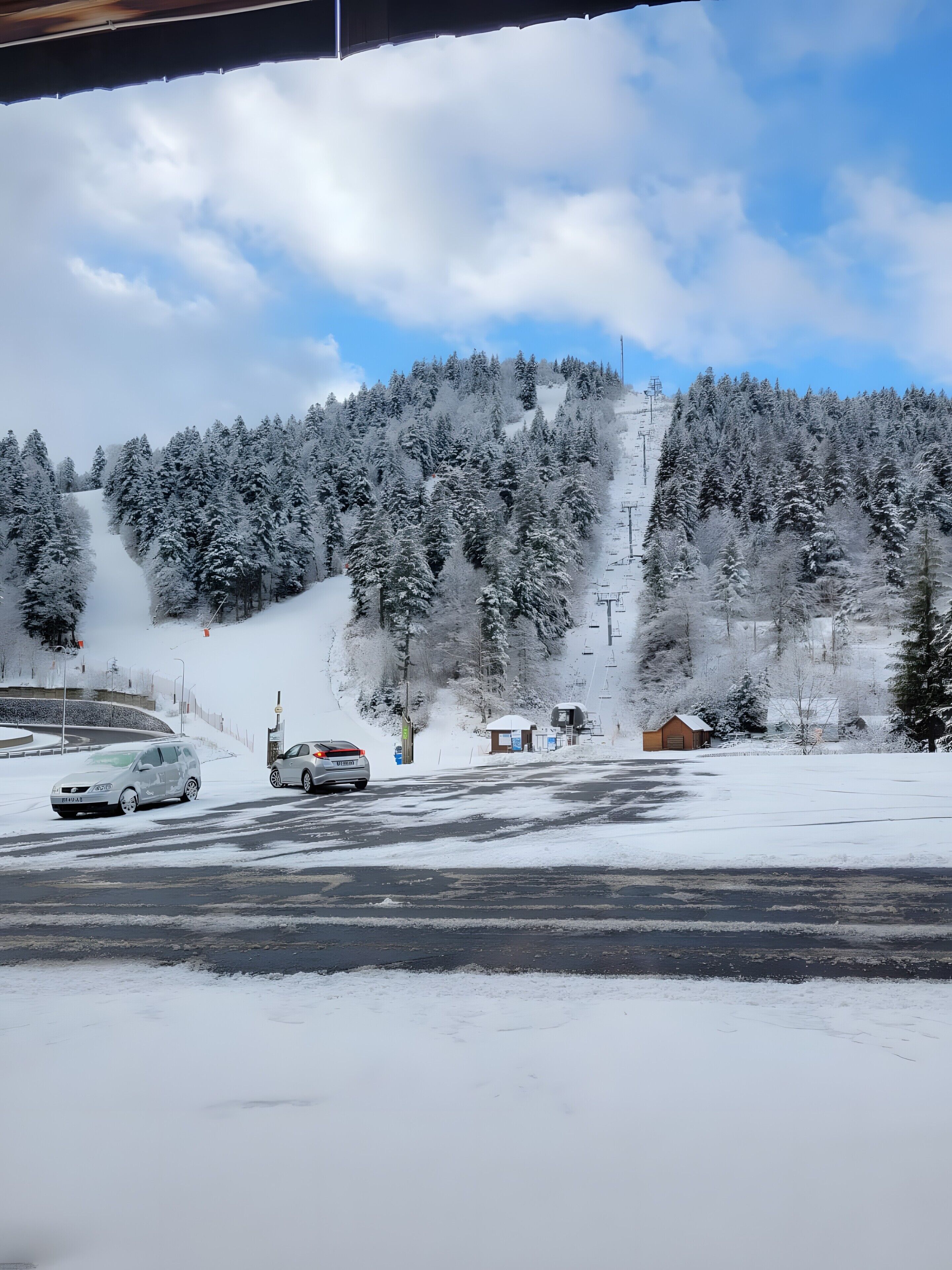 Un paysage enneigé avec une route, des voitures et une colline boisée.