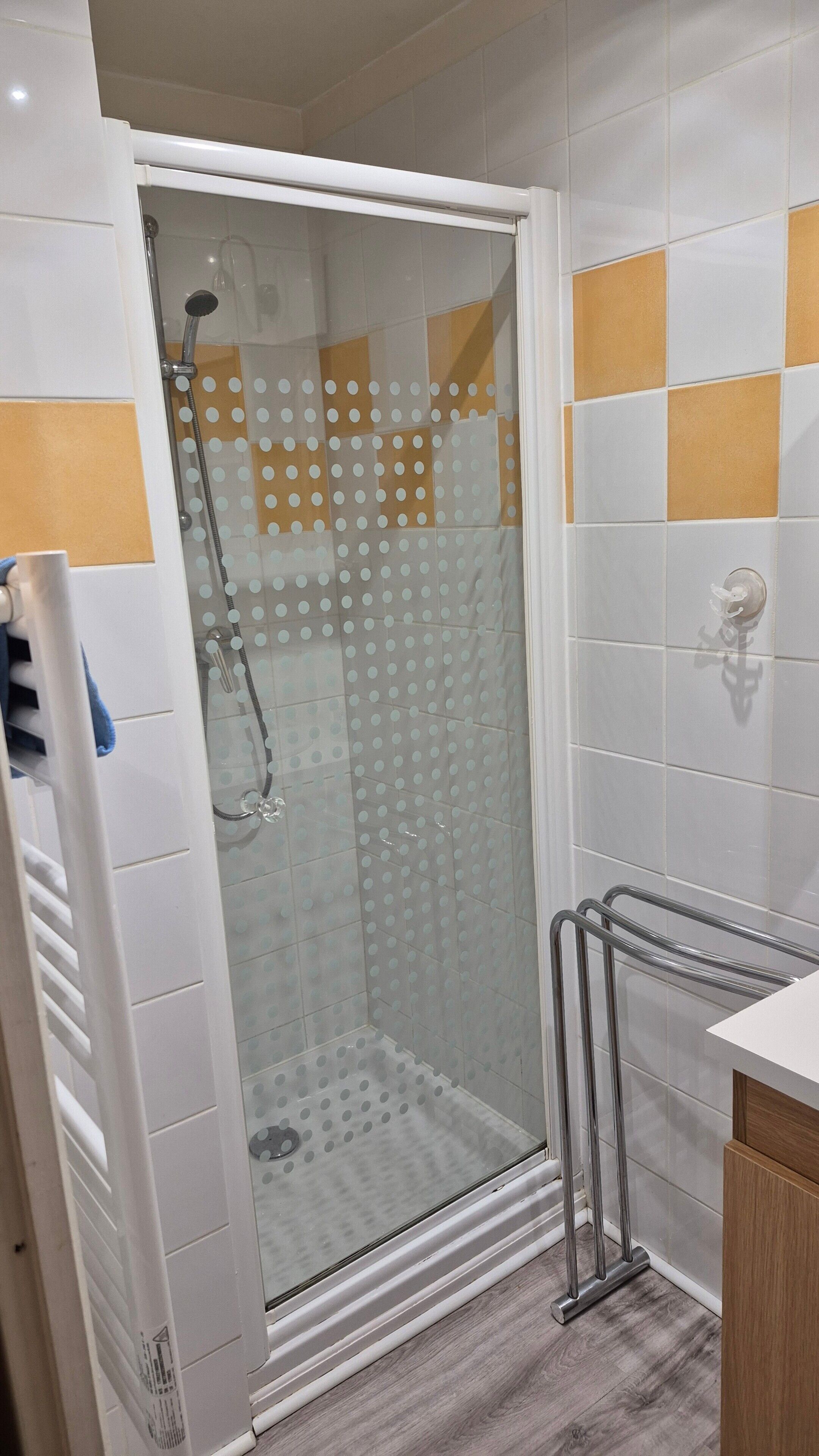 Un espace de douche doté d’une porte en verre, d’une barre d’appui en métal et d’un mur carrelé orné d’un motif à pois.