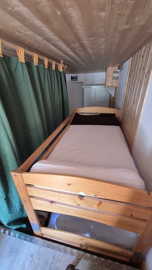 A wooden bunk bed with a mattress, a green curtain, and a small kitchenette area.