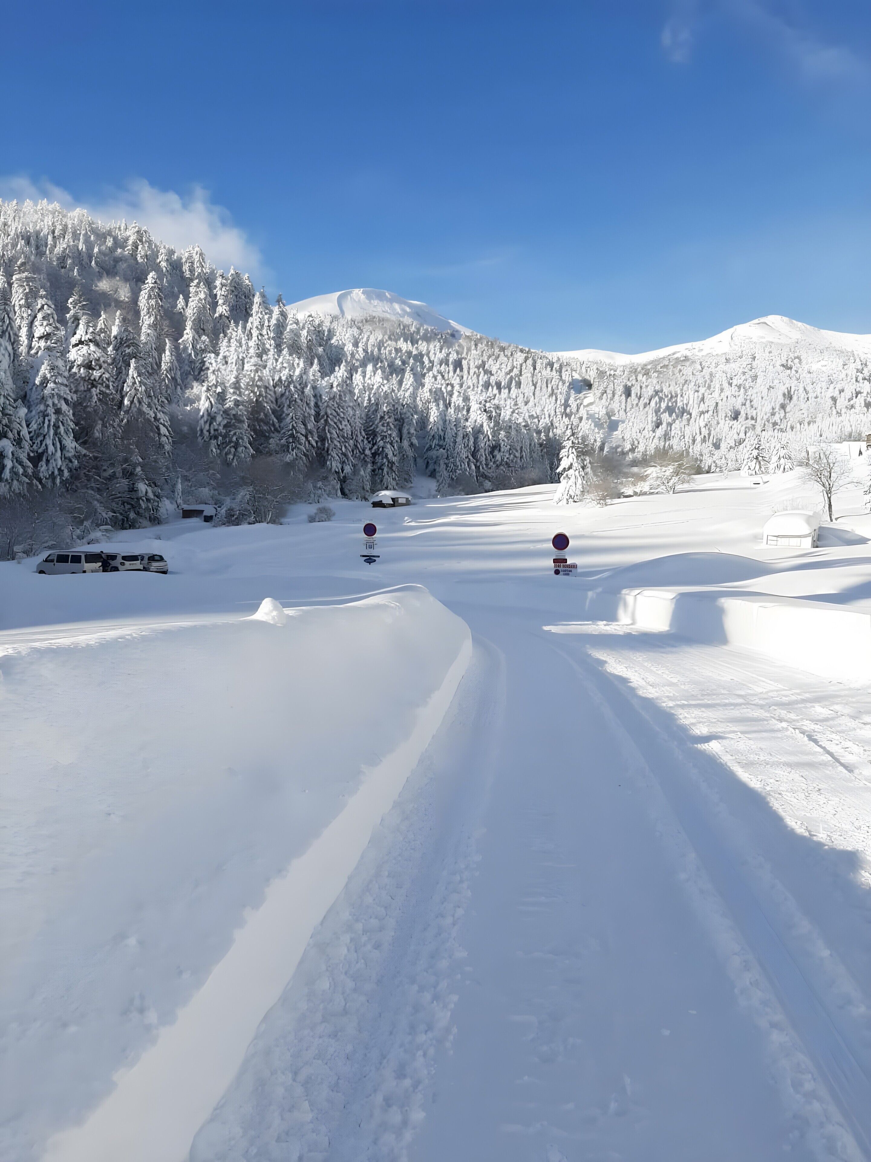 A snow-covered landscape with a clear sky, a road, and a mountain in the background.