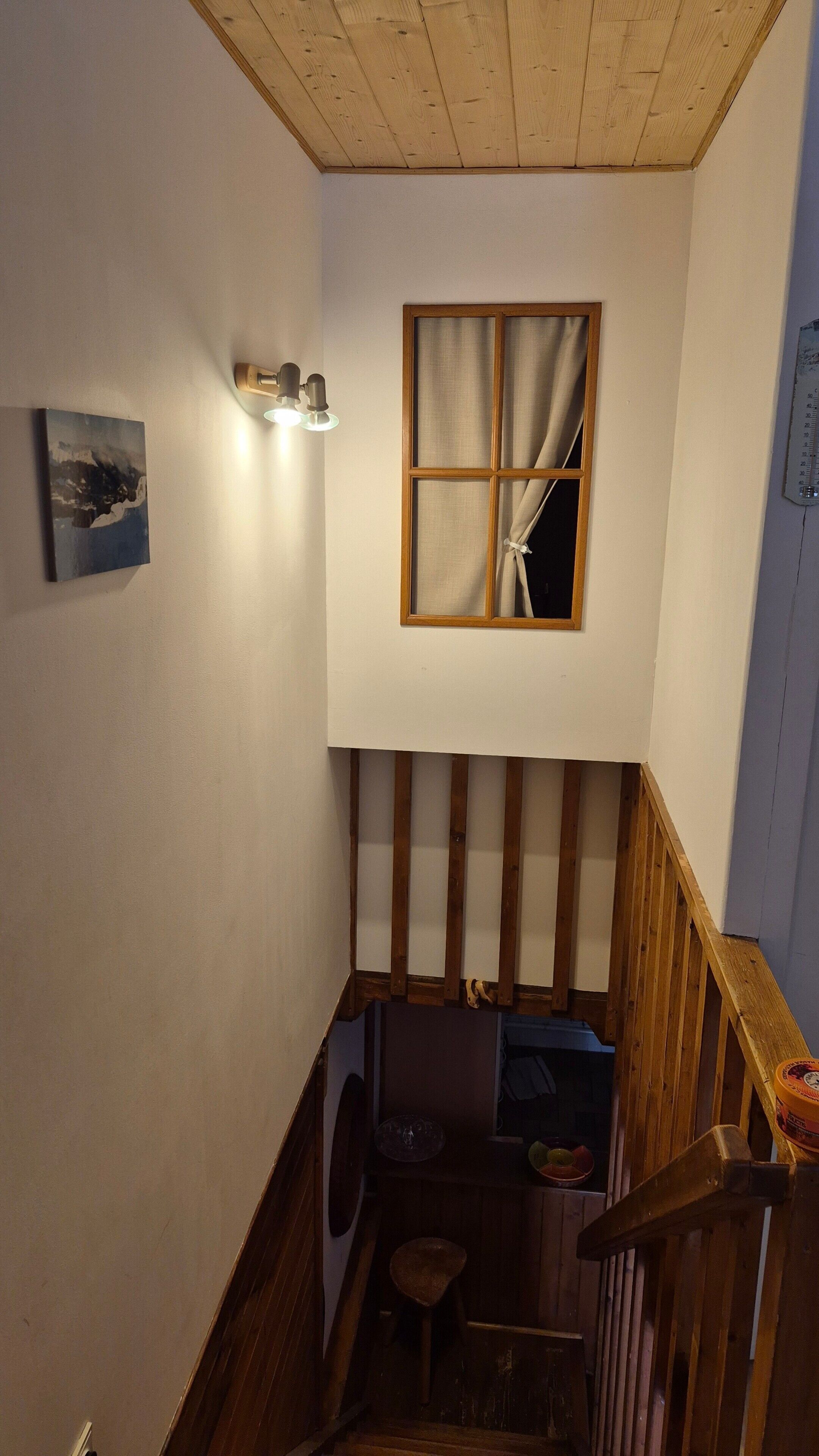 Een trap met houten leuningen die uitkomt op een plateau met een raam en een wandlamp.