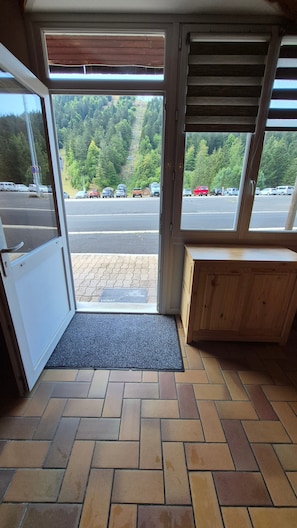 Una habitación con un banco de madera, suelo de baldosas y vistas a un estacionamiento y árboles a través de una ventana.