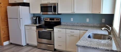 A compact kitchen with white cabinets, a stainless steel oven, a microwave, a toaster, and a sink.