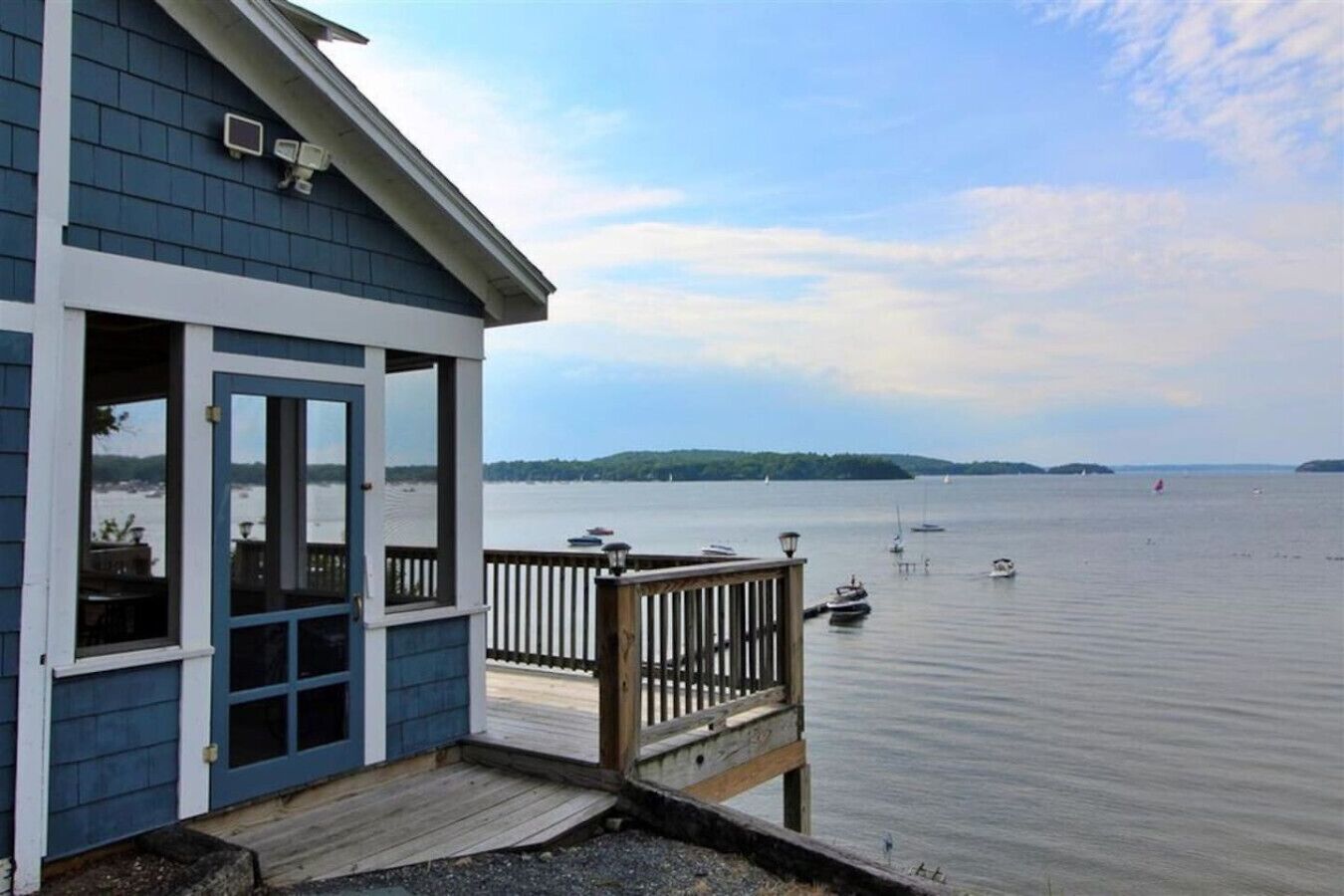 A waterfront property with a deck overlooking a calm body of water, boats, and distant land.