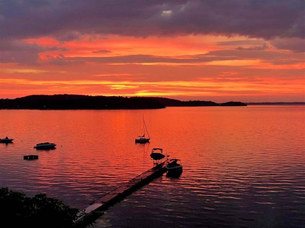 Ein Sonnenuntergang über ruhigem Wasser mit Booten, die an einem Steg vor Anker liegen.
