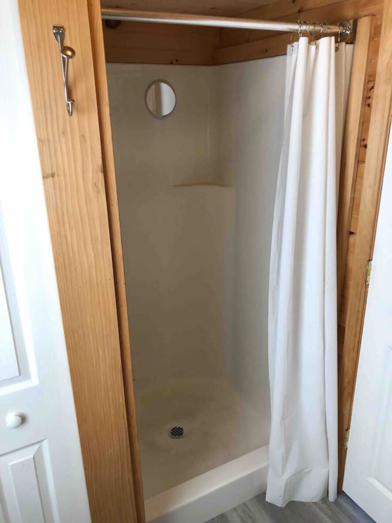 Un espace de douche doté d’un cadre de porte en bois, d’un rideau de douche et d’un miroir rond.