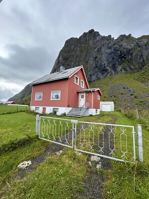Een rood huis met een witte deur en ramen, een trap en een metalen hek ervoor.