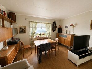 Een gezellige woonkamer met een eethoek, houten meubels, een televisie en uitzicht door het raam.