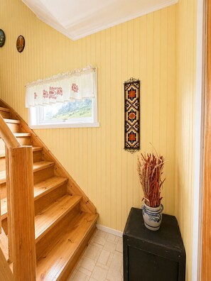 A wooden staircase leading to a room with yellow walls, a window with a view of greenery, and a decorative wall hanging. - Midnight Sun House in Eggum, Lofoten (Vestvågøy)