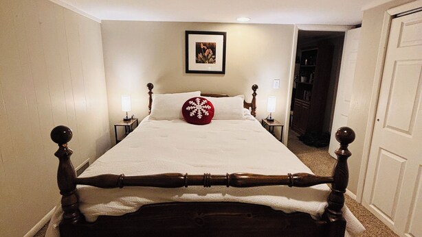 A bedroom with a large bed, a ceiling light, a framed picture on the wall, and a door to the right.