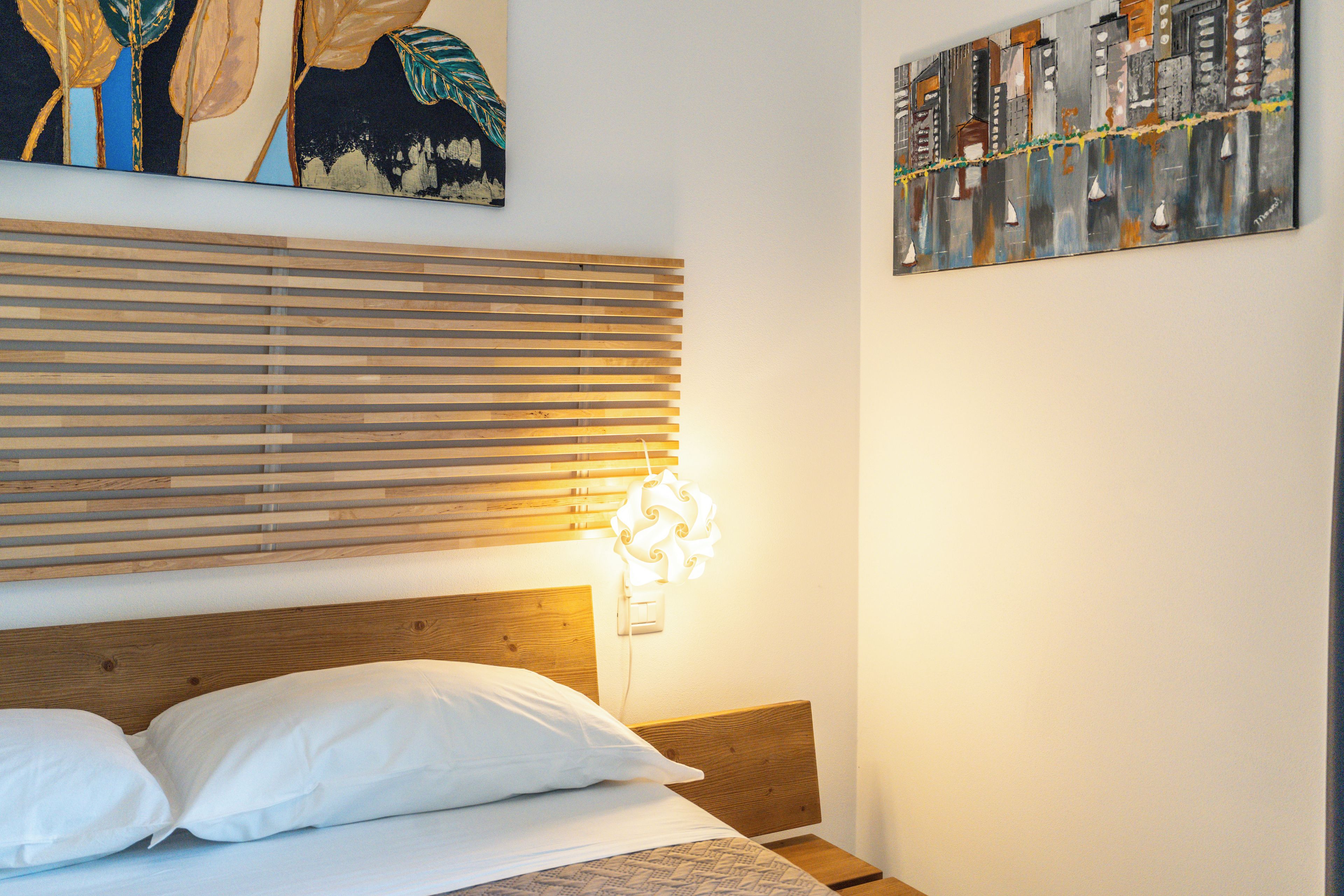 A bedroom with a wooden headboard, a bed with white bedding, and a wall-mounted light fixture.