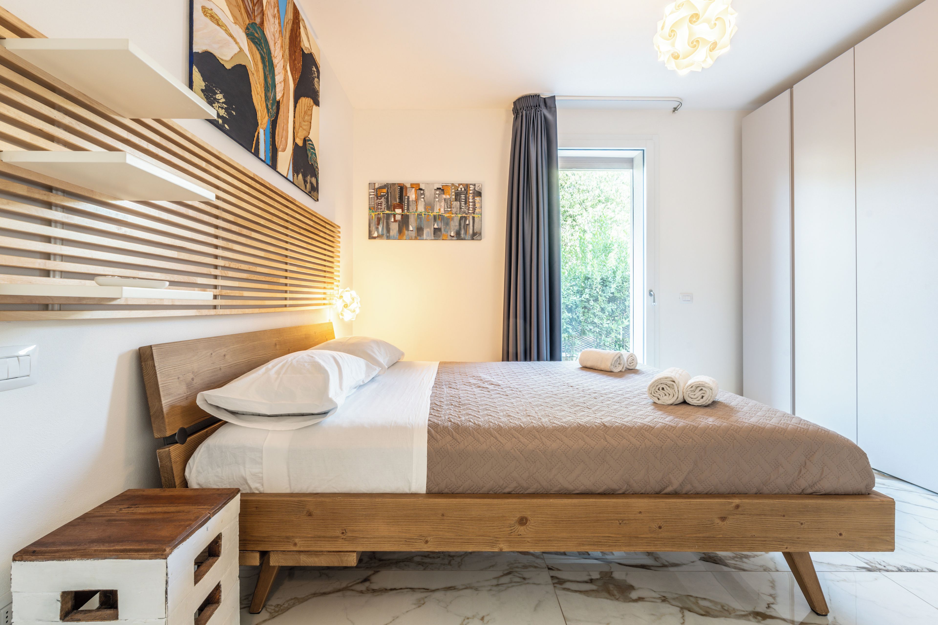 A modern bedroom with a wooden bed, a nightstand, a wall-mounted shelf, and a window with curtains.