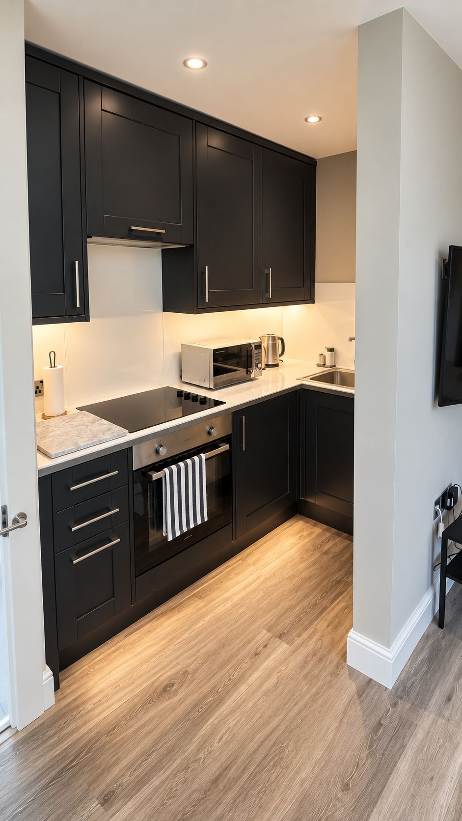 A modern kitchen with dark cabinetry, a microwave, a kettle, and a stove.