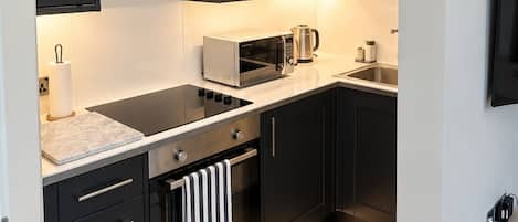A modern kitchen with dark cabinetry, a microwave, a kettle, and a stove.