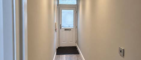 A hallway with a door at the end, a window above the door, and a light switch on the wall.