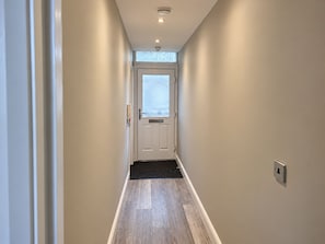 Ein Flur mit einer Tür am Ende, einem Fenster darüber und einem Lichtschalter an der Wand.