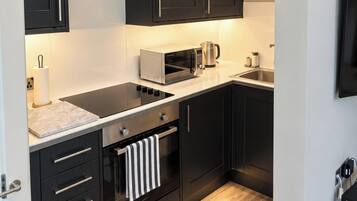 Une cuisine moderne avec des meubles de rangement aux couleurs sombres, un four à micro-ondes, une bouilloire et un évier en acier inoxydable.