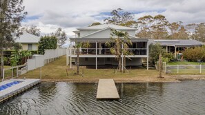 A two-story house with a balcony, a swimming pool with a wooden dock, and a fenced yard. - Holiday Mode | Lakefront Luxury with private jetty (Lake Conjola)