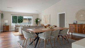 A spacious living area with a large wooden dining table surrounded by chairs, a sofa, and a side table with a lamp. - Holiday Mode | Lakefront Luxury with private jetty (Lake Conjola)