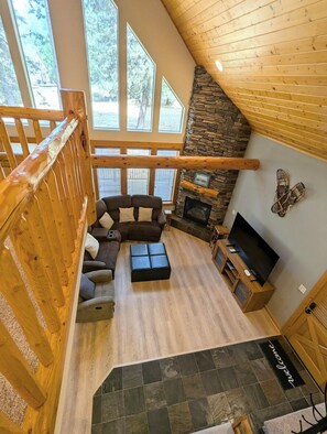 A spacious living area with a stone fireplace, a large window, and a wooden staircase.