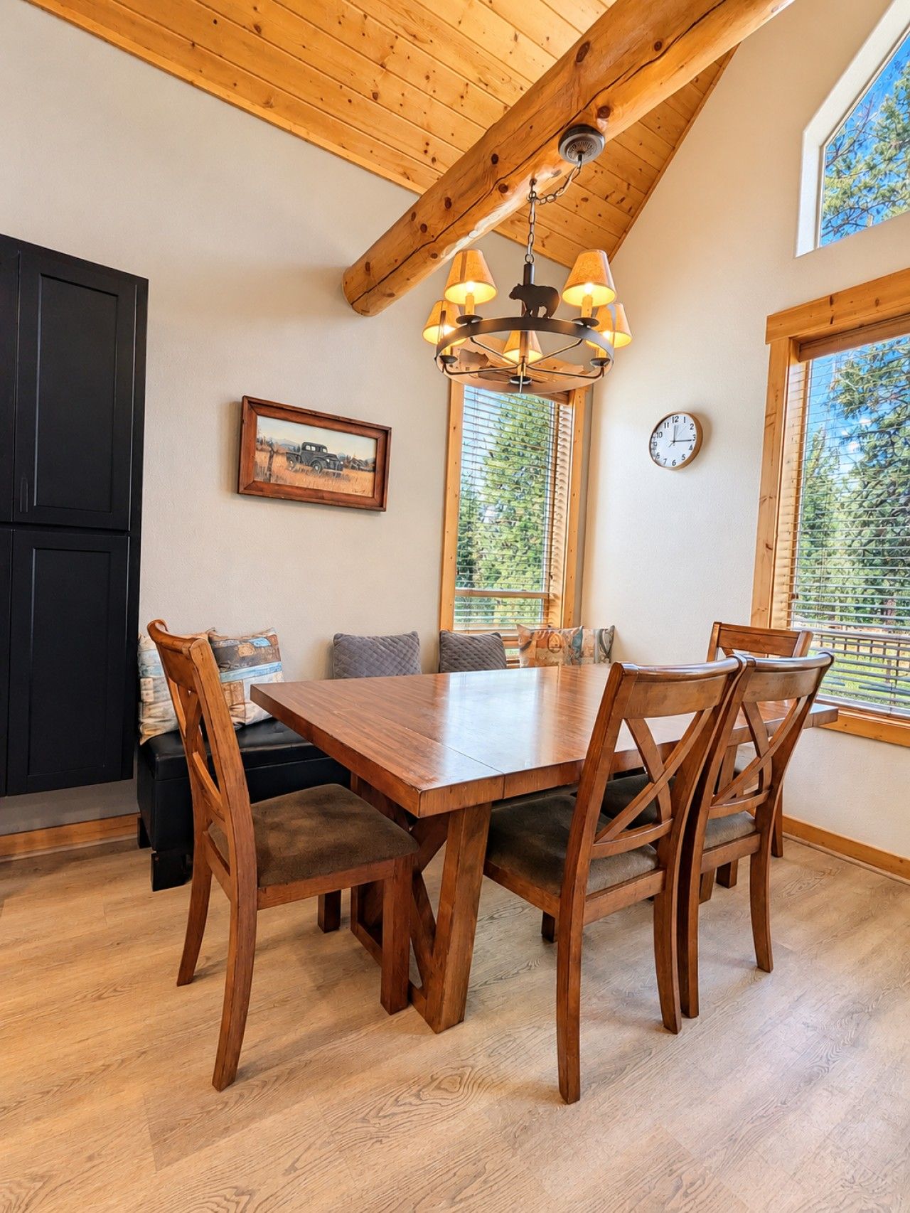 A dining area with a wooden table and chairs, a ceiling fan, a clock, and a window with blinds.