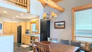 A spacious kitchen with wooden cabinets, a dining area with a wooden table and chairs, and a lofted seating area with a view. - Harrier Pine Chalet At The Running Y (Klamath Falls)