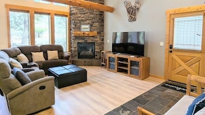 A cozy living room with a stone fireplace, a flat-screen TV, and a wooden ceiling. - Harrier Pine Chalet At The Running Y (Klamath Falls)