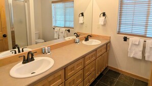 A bathroom with two sinks, a mirror with lights, wooden cabinets, and a shower. - Harrier Pine Chalet At The Running Y (Klamath Falls)