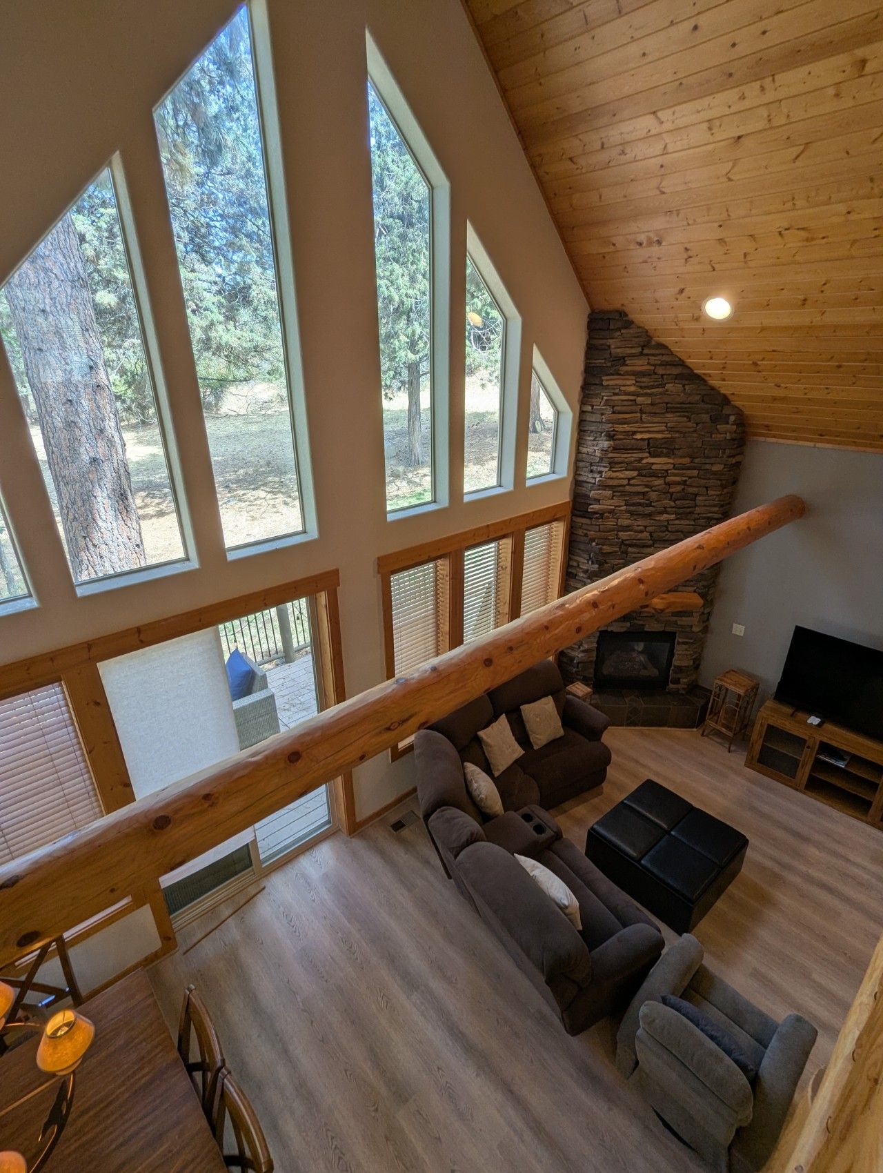A spacious living room with a stone fireplace, large windows, and a wooden ceiling.