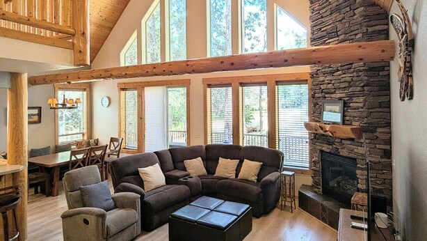 A spacious living room with a large sectional sofa, a fireplace, and a high ceiling with wooden beams. - Harrier Pine Chalet At The Running Y (Klamath Falls)