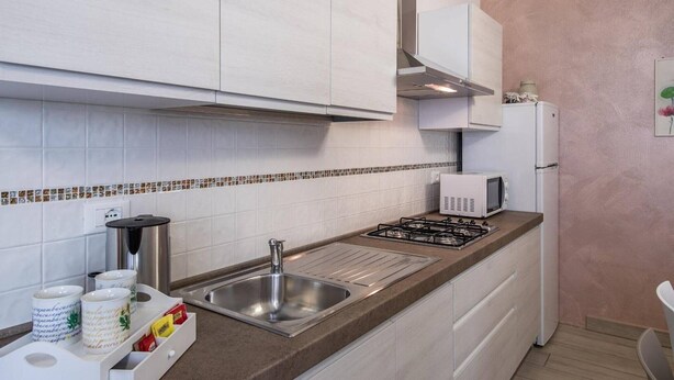 A modern kitchen with white cabinets, a stainless steel sink, a gas stove, and a white refrigerator.