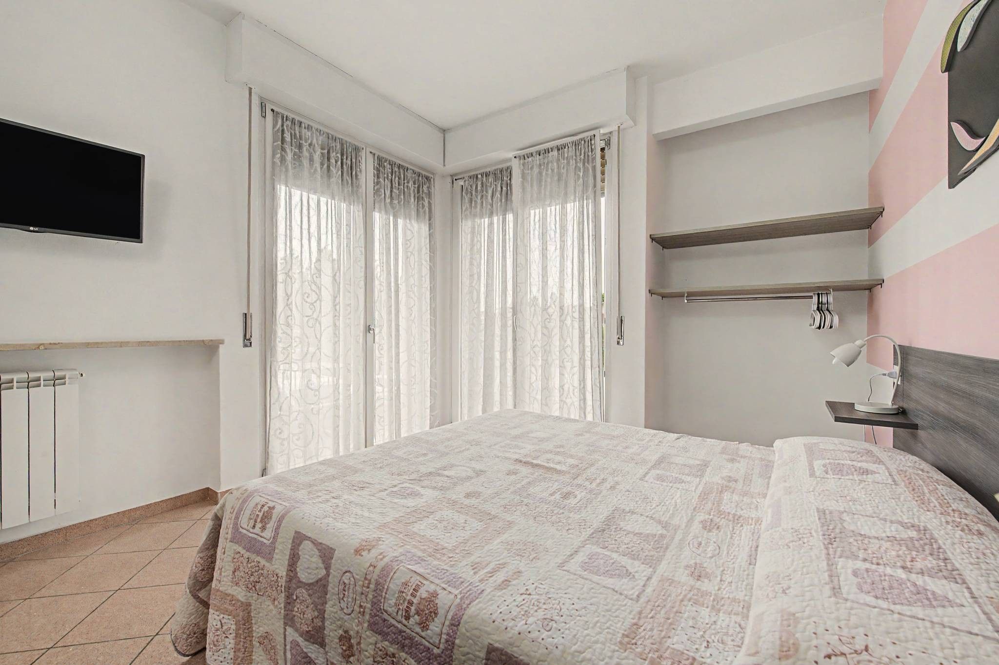 A bedroom with a bed, a TV mounted on the wall, and a radiator.