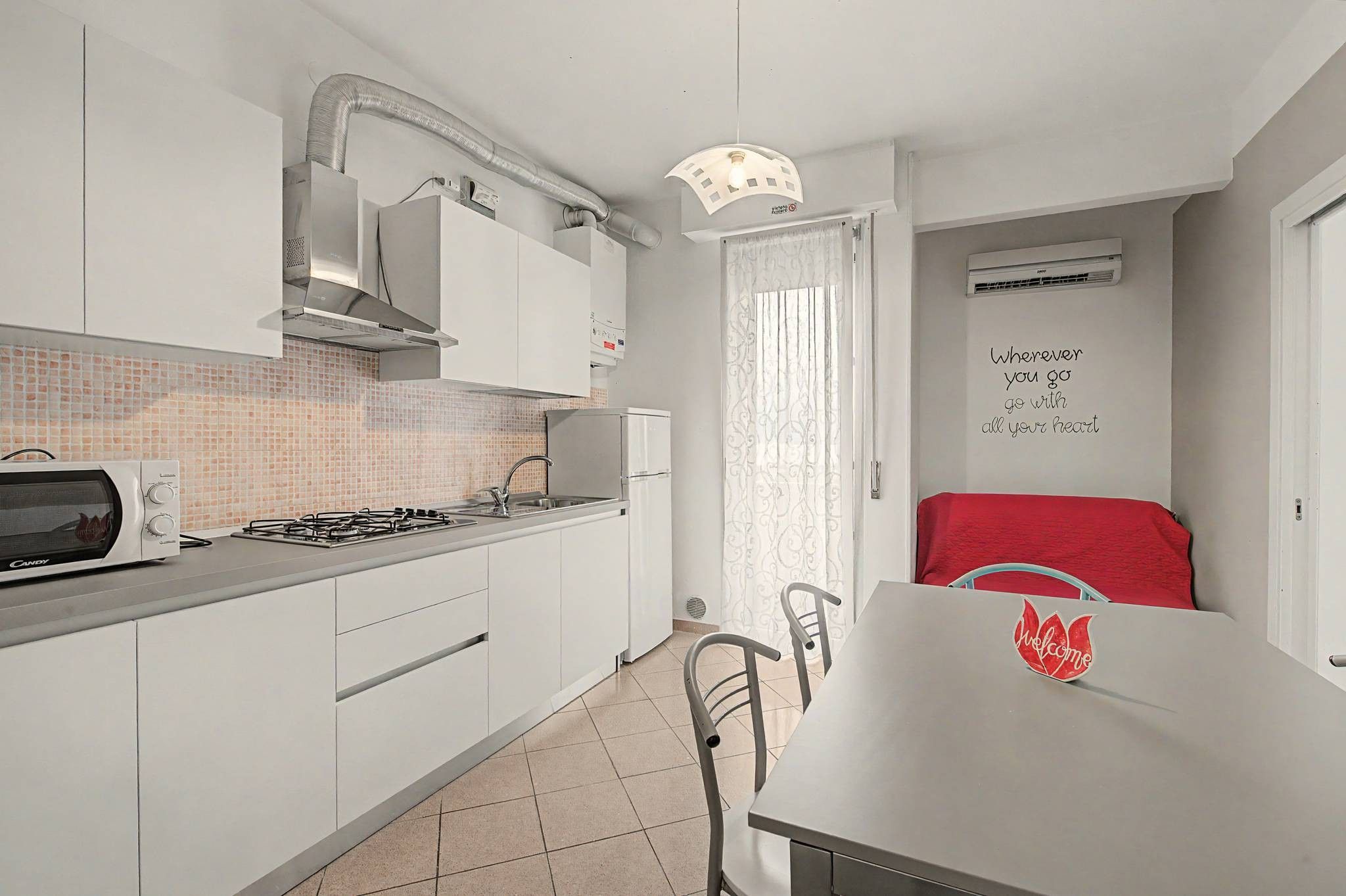 A modern kitchen with white cabinets, a gas stove, a microwave, and a ventilation hood.