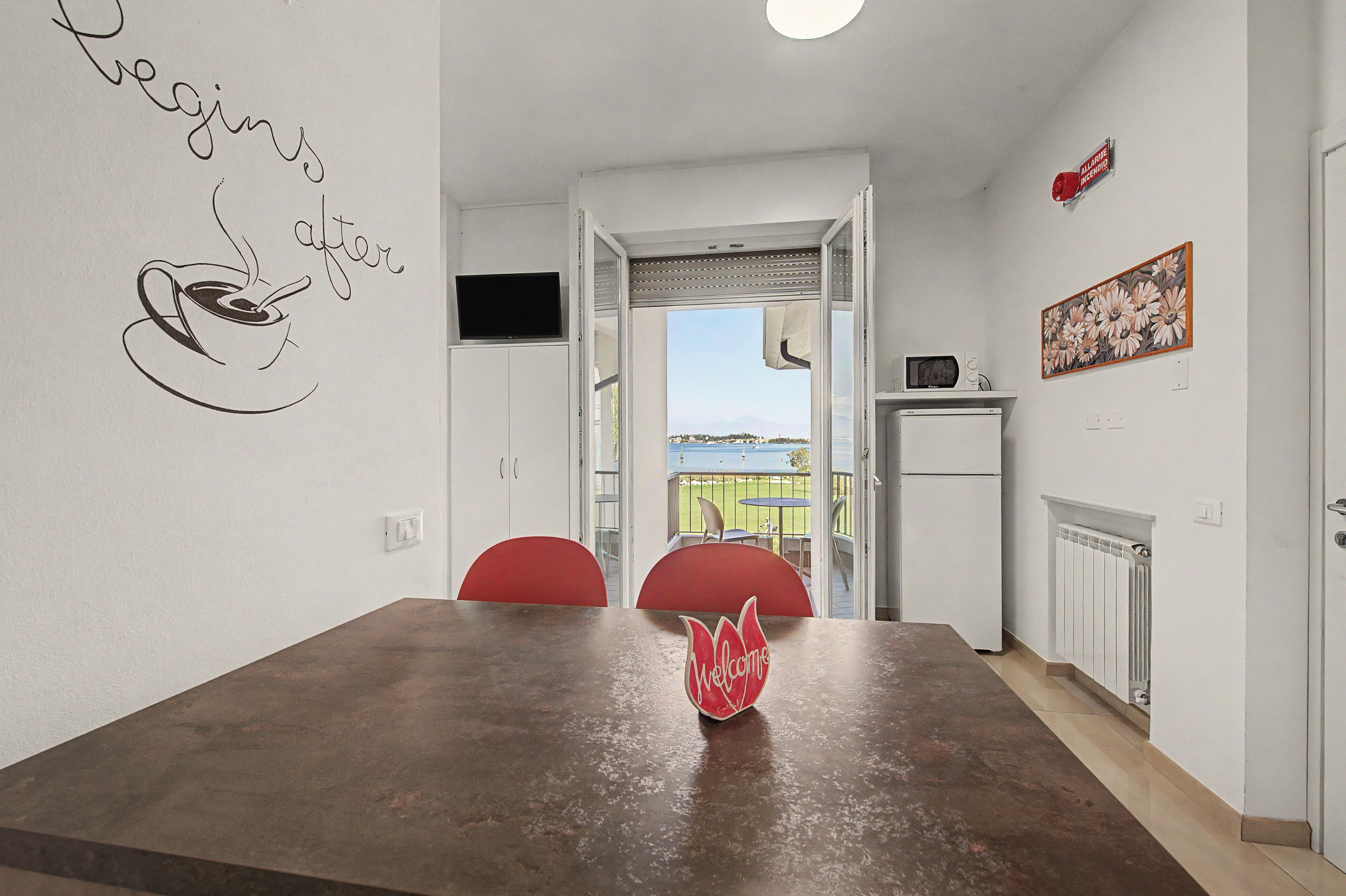 Ein Essbereich mit Tisch, Stühlen, einem Willkommensschild, einem Fernseher und Blick ins Freie.