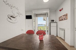 A dining area with a table, chairs, a welcome sign, a TV, and a view of the outdoors. - Margherita - Open Space Lake View Apartment with Lake View, Wi-Fi, and Air Conditioning (Sirmione)