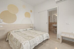 Ein Schlafzimmer mit Bett, Nachttisch, Wand-Klimaanlage und angrenzendem Badezimmer.