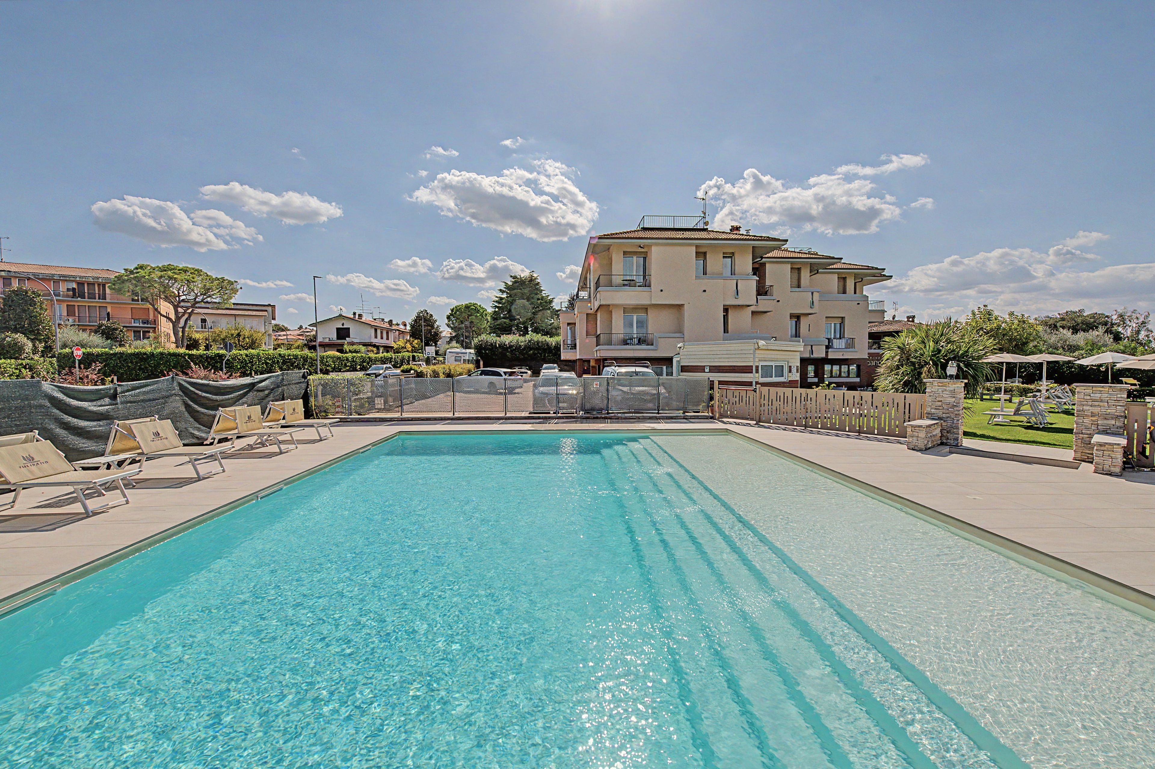 Ein rechteckiger Pool mit klarem Wasser, umgeben von Liegestühlen und einem Zaun.