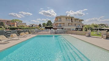 Ein rechteckiger Pool mit klarem Wasser, umgeben von Liegestühlen und einem Zaun.