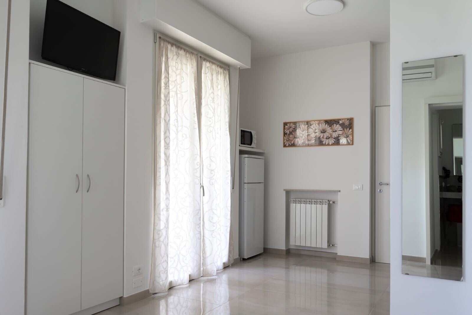 A spacious room with a large wardrobe, a microwave, a radiator, and a painting on the wall.