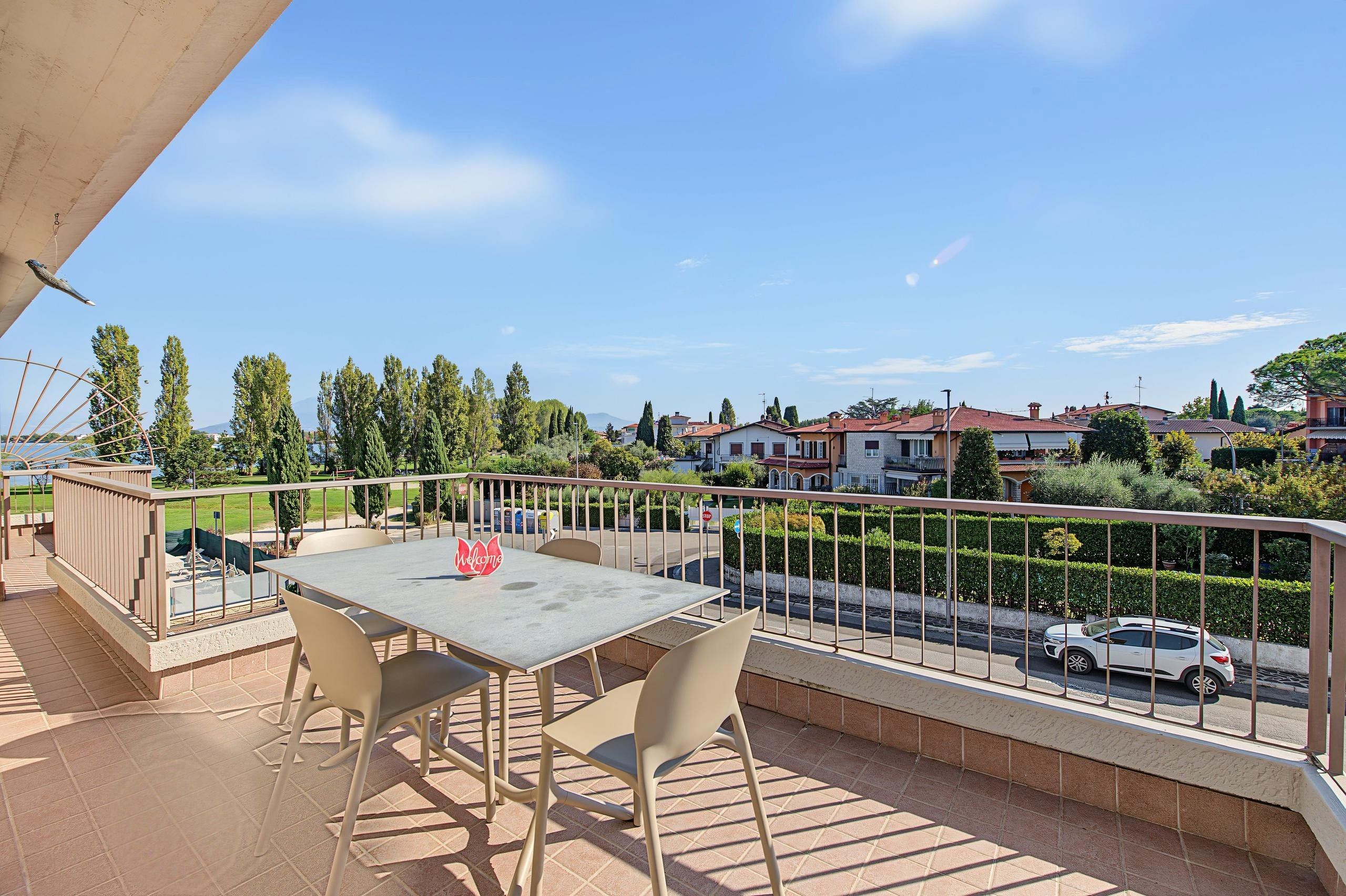 A balcony with a table and chairs, overlooking a residential area with houses and a road.